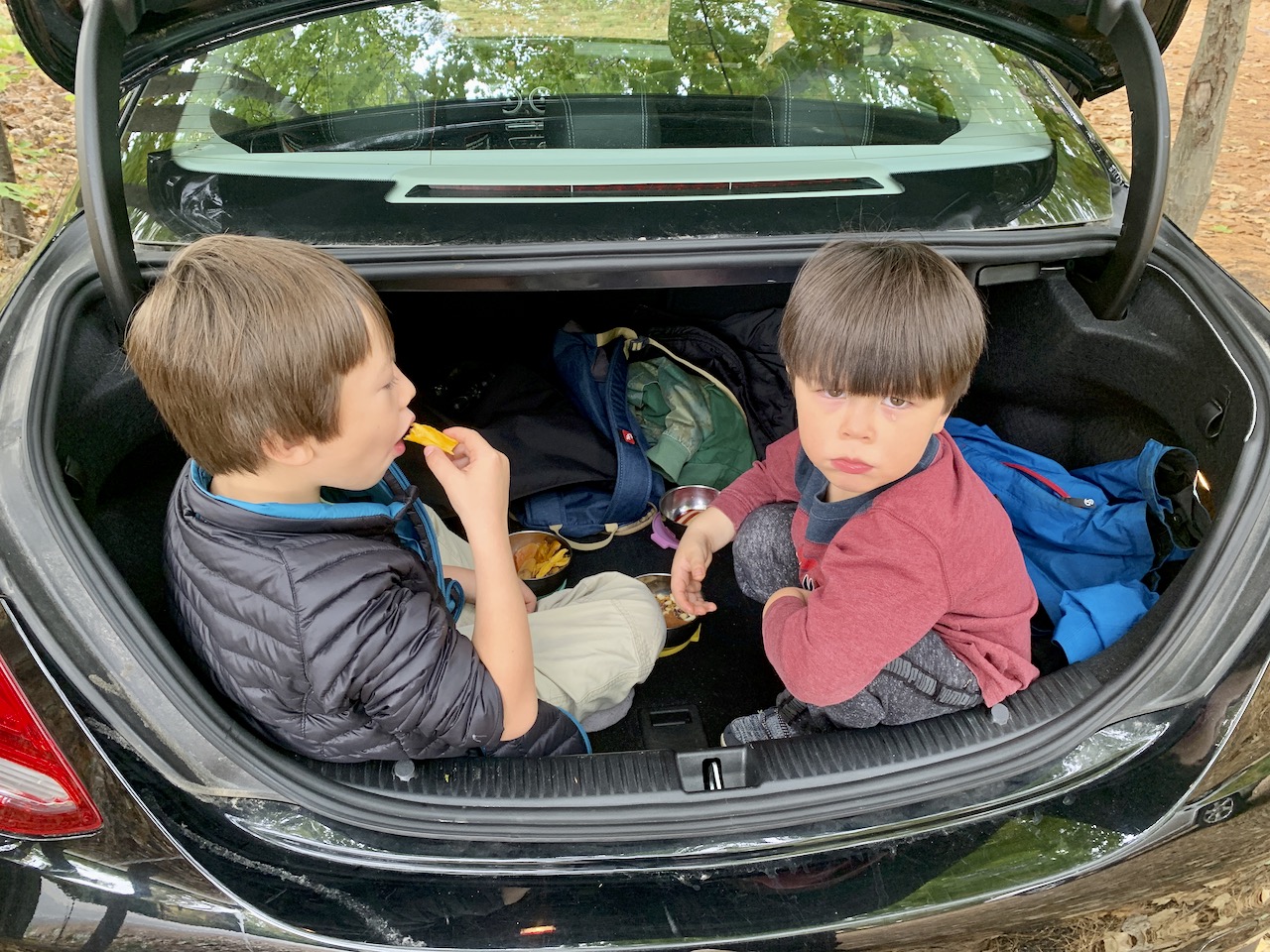 Two kids eating snacks in a car trunk